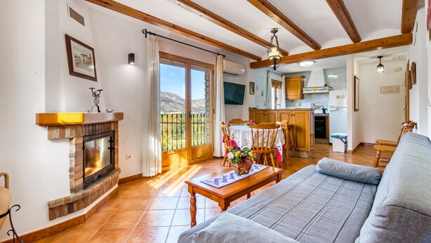 Una sala de estar con chimenea, un sofá, una mesa de comedor con sillas y una cocina al fondo.