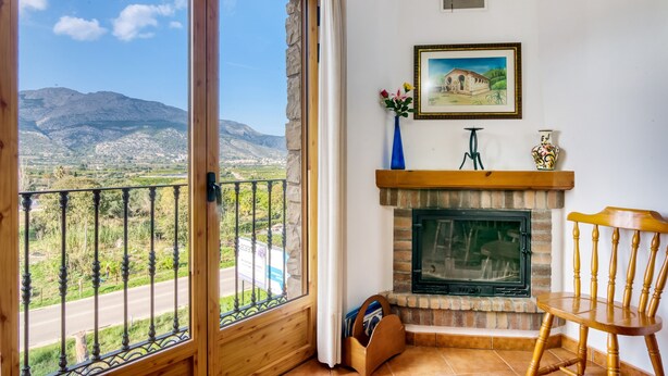 Une pièce avec une cheminée, une chaise en bois, un tableau encadré et une vue sur les montagnes, visible à travers une porte vitrée.
