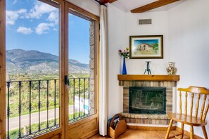 Habitación con chimenea, una silla de madera, un cuadro enmarco y vistas a las montañas a través de un ventanal.