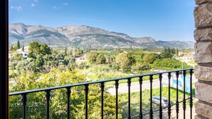 Een balkon met uitzicht op bergen, groen en een weg met auto's.