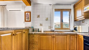 Een keuken met houten kastjes, een granieten aanrecht, een raam met uitzicht en een witte betegelde spatwand.