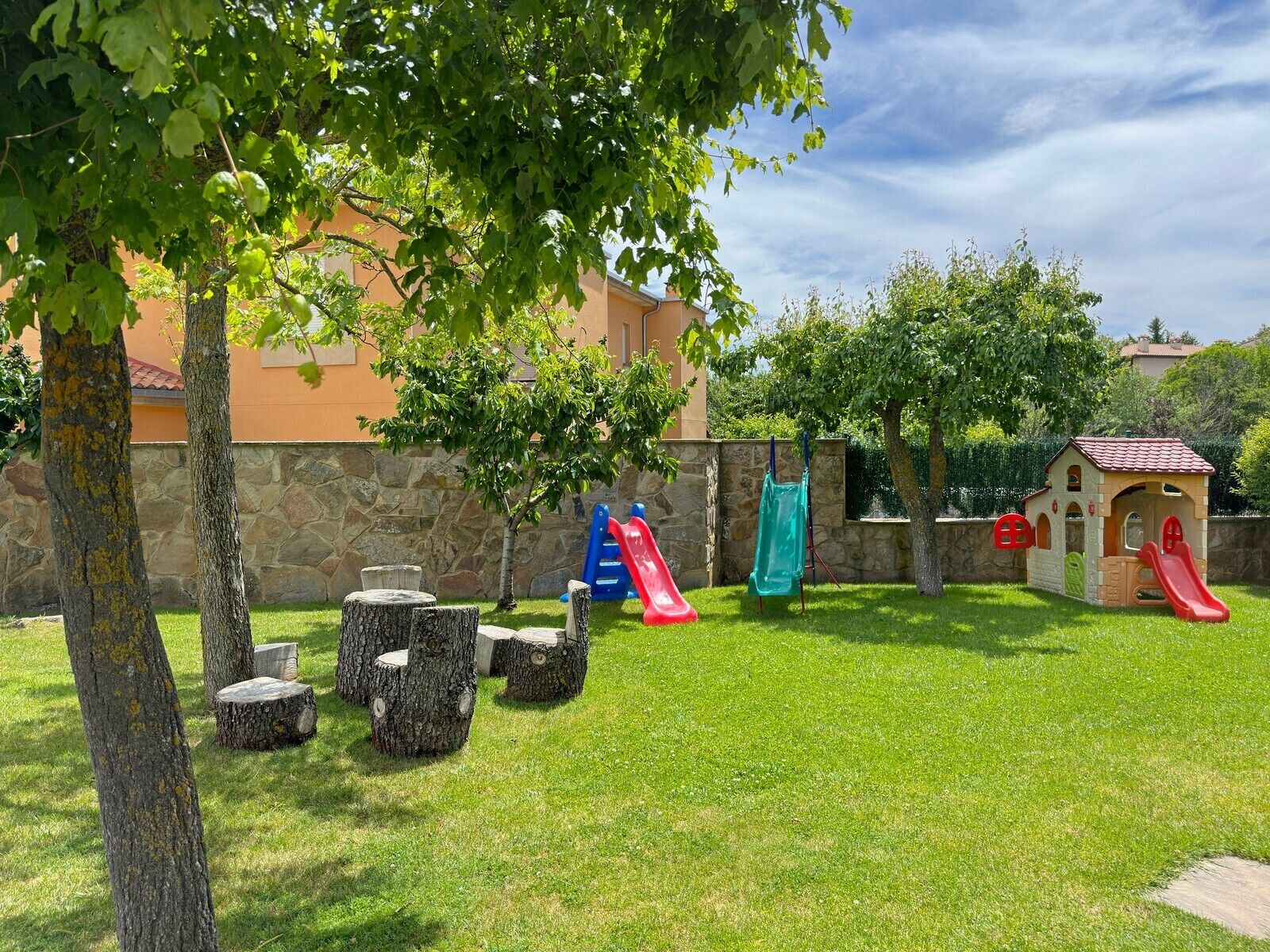 A grassy outdoor area with a play structure, a small building, and stone walls.