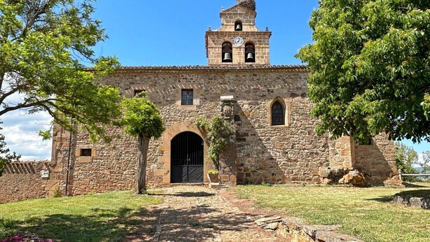Un edificio histórico de piedra con una torre de campanas, una entrada en arco y un camino empedrado que conduce a la puerta.