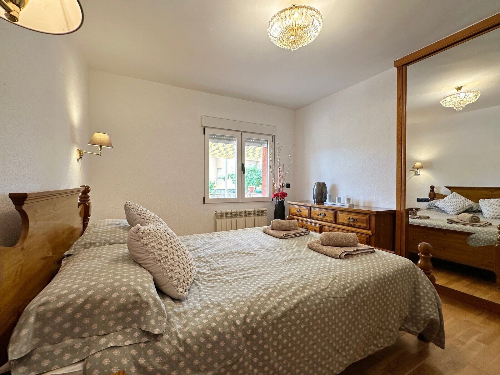 Une chambre avec deux lits, une commode, un miroir, une fenêtre donnant sur un beau paysage et un lustre.