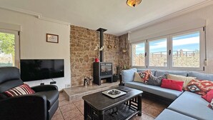 Una sala de estar con pared de piedra, chimenea, sofá, televisor y vista al mar.
