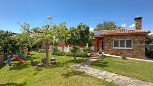 Una casa de piedra con techo de tejas, un pequeño patio y un parque infantil con toboganes.