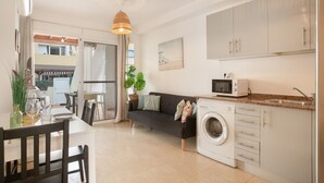 Een kleine keuken met een wasmachine, een magnetron en een eethoek met een tafel en stoelen.