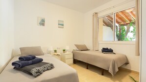Slaapkamer met twee bedden, een nachtkastje met lamp, een raam met uitzicht op groen en een plafondventilator.