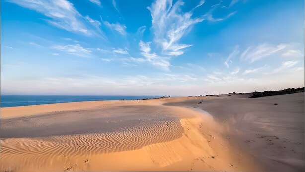 Een uitgestrekt woestijnlandschap met golvende zandduinen en een heldere blauwe lucht.
