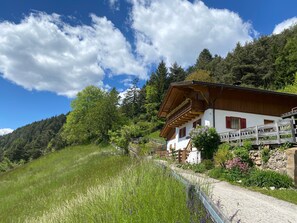 Een klassiek chalet met een houten balkon, omgeven door weelderige begroeiing en een heldere lucht.