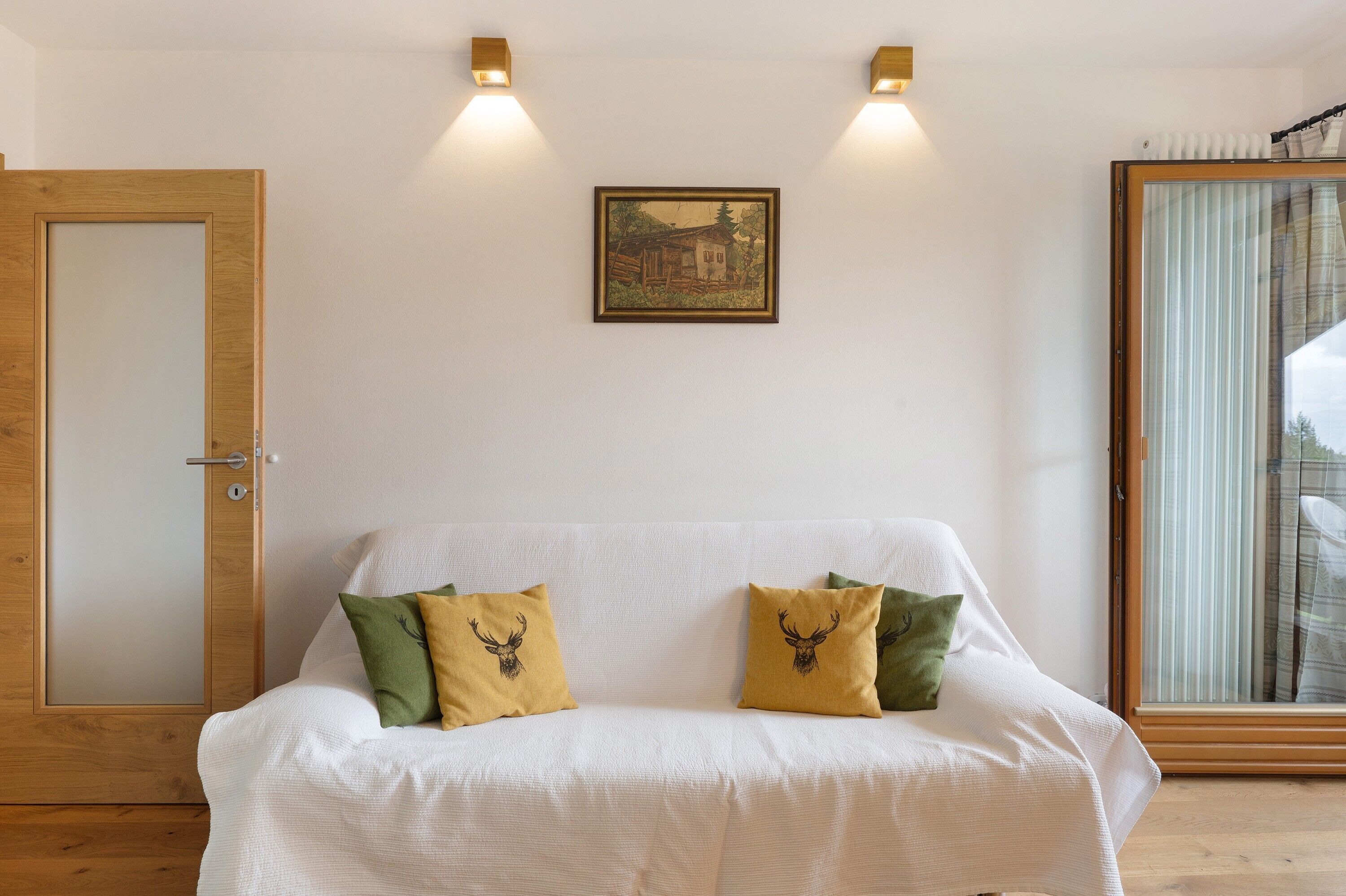 A white sofa with two decorative pillows, a framed picture on the wall, and a wooden door.