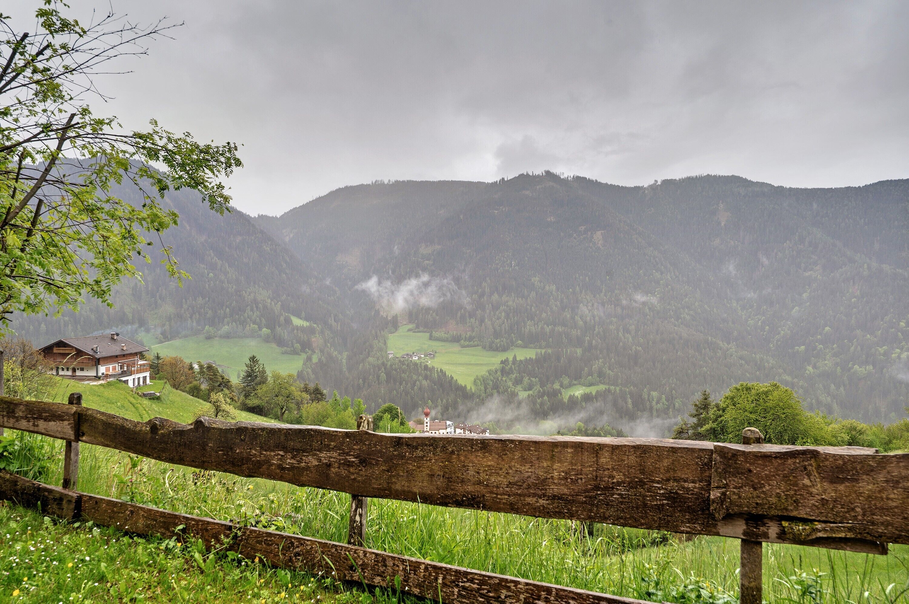 Un paysage de montagne avec une clôture en bois, une maison et une vallée.