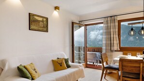 A cozy room with a white sofa, a dining table with chairs, and a large window with a view of mountains. - Apartment 'Leitner' with Mountain View, Private Terrace and Wi-Fi (Tiers)