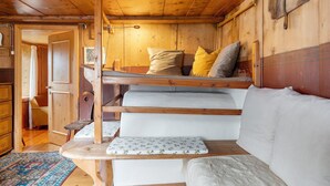 Interior de una cabaña de madera con una cama litera, un sofá y una pequeña mesa.
