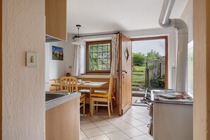 A kitchen with a dining table, chairs, a refrigerator, and a window with curtains.