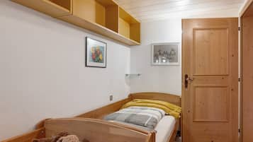 A bedroom with a wooden bed, a shelf above the bed, and a door.