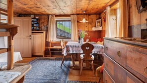 Un interior de madera con una mesa de comedor, sillas, un tapete, un aparador y una ventana con cortinas.