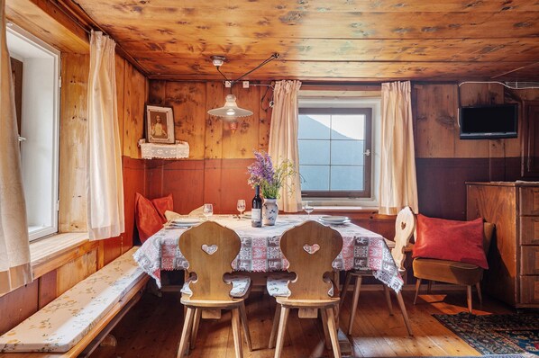 A dining area with a wooden table, chairs, a bench, a television, and a window with curtains.