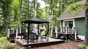 Une terrasse en bois avec un belvédère, des sièges d’extérieur et un escalier menant à un bâtiment.