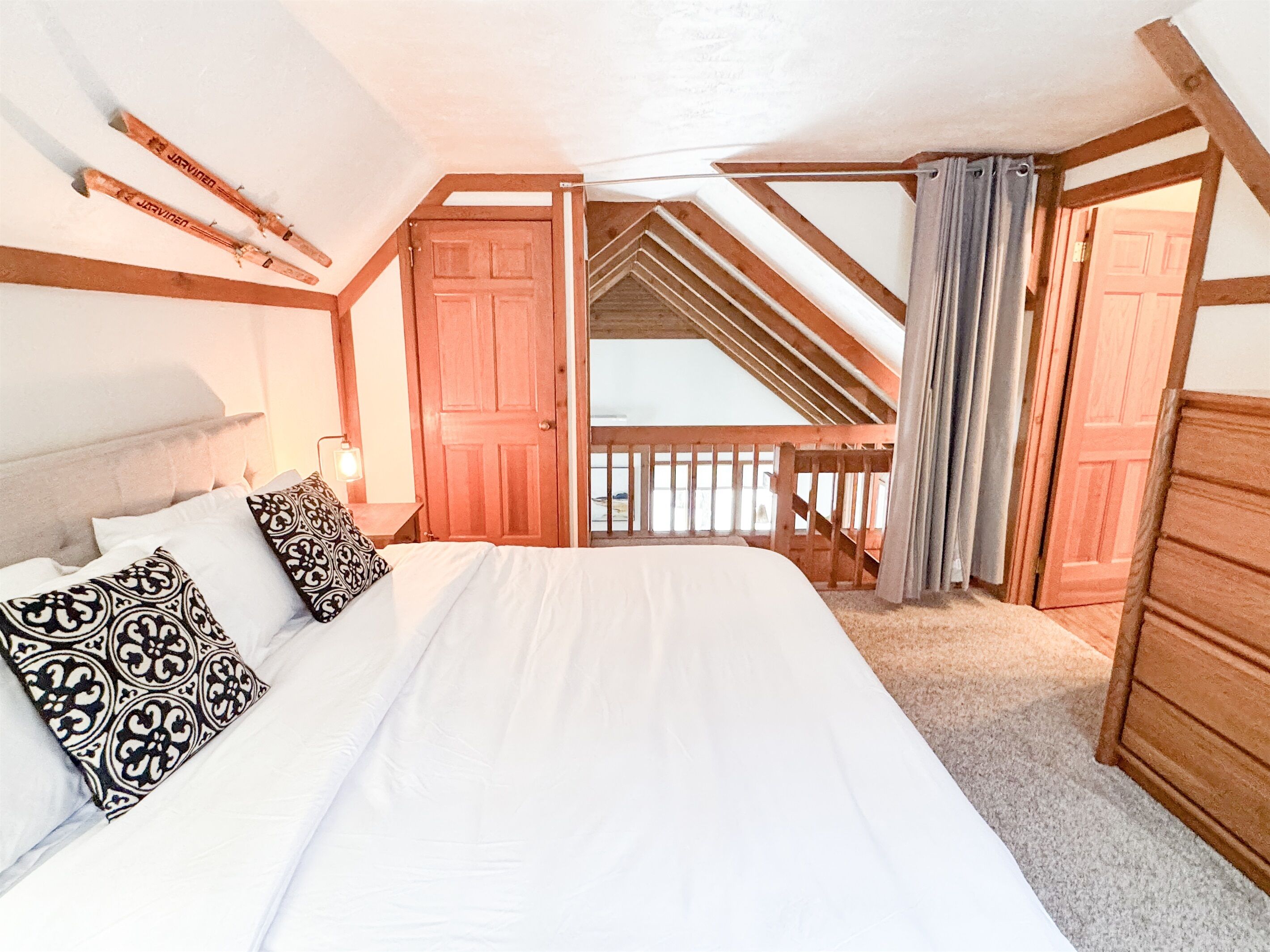 A bedroom with a large bed, wooden ceiling beams, a wooden door, and a view of the outside.
