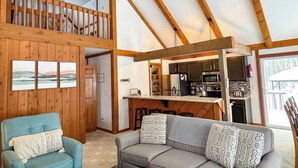 Un vaste espace de vie de style loft, doté d’un plafond haut, de poutres apparentes, d’une cuisine équipée d’appareils modernes et d’un coin salon confortable avec un canapé et un fauteuil.