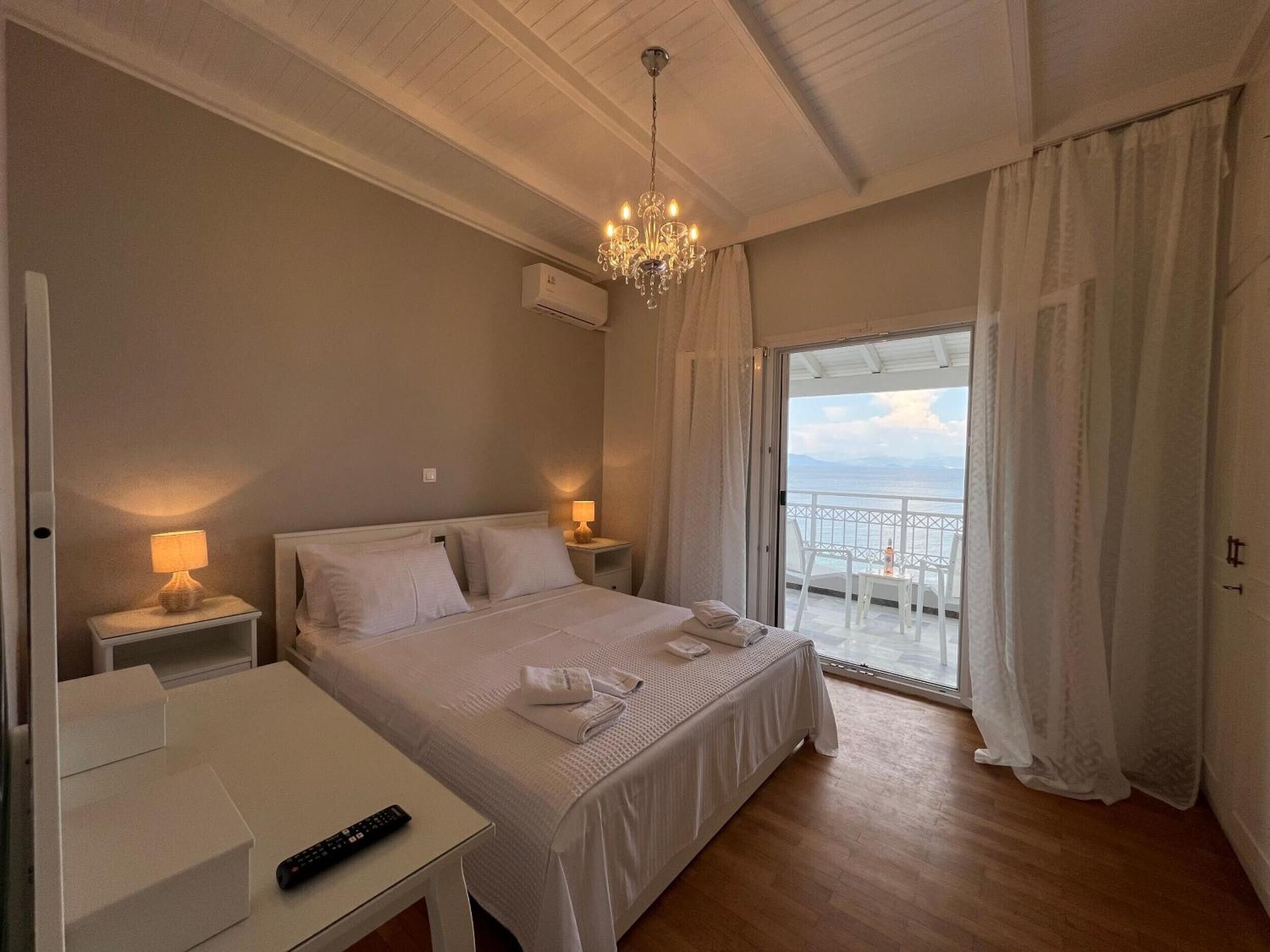 Une chambre d’hôtel avec un lit, des lampes de chevet, une télécommande, un balcon avec vue et un lustre.