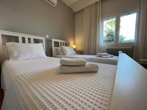 A hotel room with two beds, a window with curtains, a radiator, and a lamp.