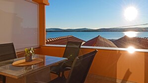 A balcony with a table and chairs, overlooking a body of water and distant mountains.