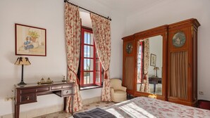 A bedroom with a bed, a desk, a chair, a wardrobe, and a window with curtains.