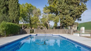A rectangular swimming pool with clear blue water, surrounded by a fence and trees.