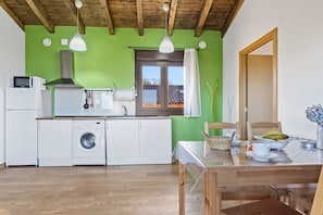 Una cocina con lavadora, microondas y ventana con vista a una casa.