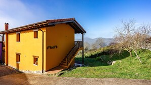 Un bâtiment jaune avec un escalier menant à un balcon, entouré d’une zone herbeuse et avec des montagnes en arrière-plan.