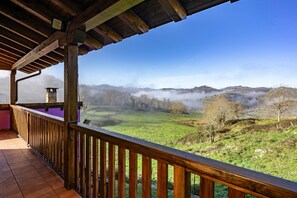 A wooden balcony with a view of a green valley and mist-covered hills.
