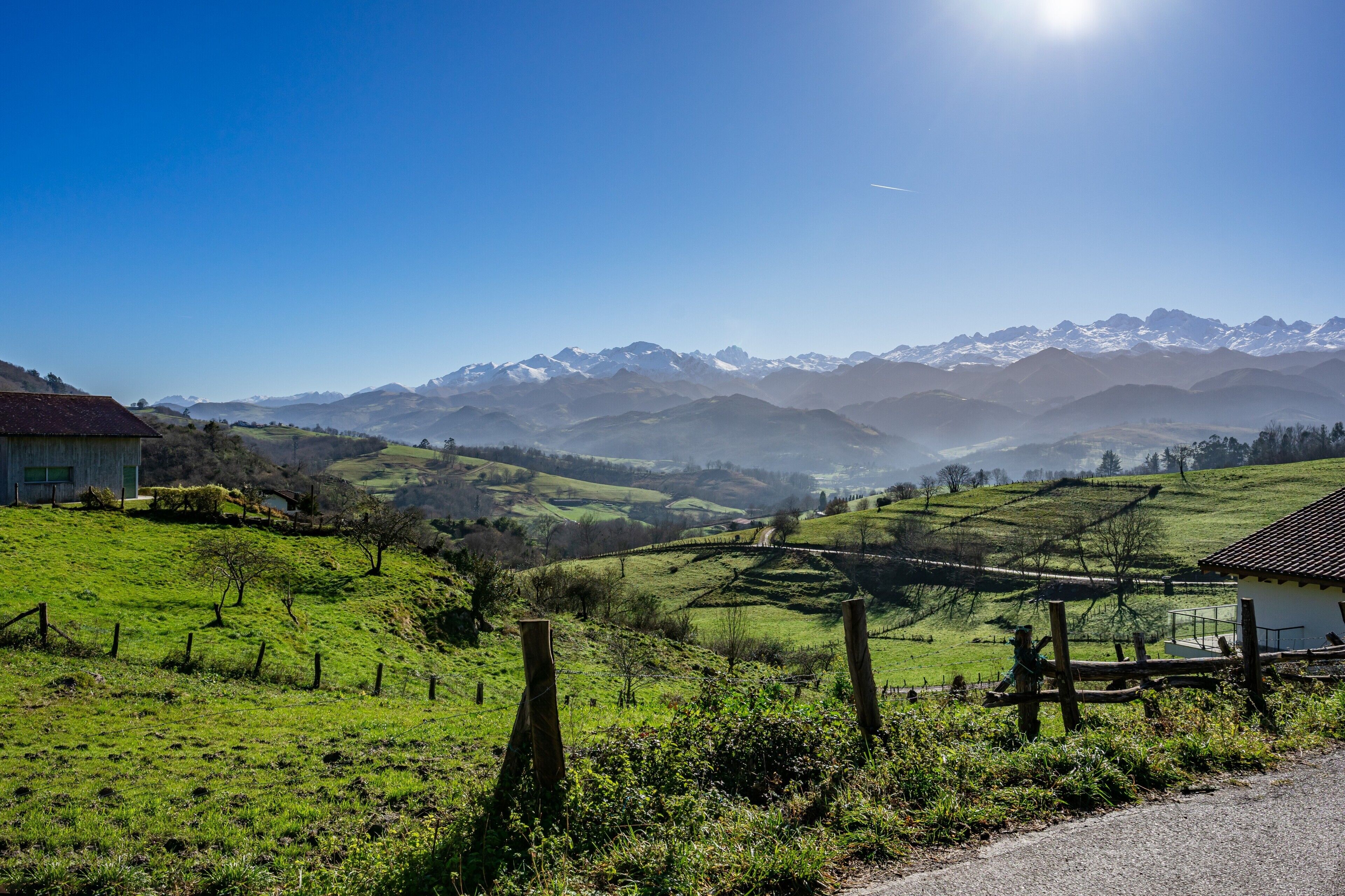 Un paysage rural avec une maison, un espace clôturé et une chaîne de montagnes en arrière-plan.