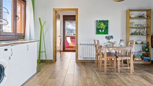 Une cuisine équipée d’un lave-linge, de meubles de rangement en bois, d’une table à manger avec des chaises, d’un radiateur et d’un luminaire suspendu.
