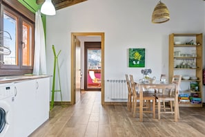 Una cocina con lavadora, armarios de madera, una mesa de comedor con sillas, un radiador y una lámpara colgante.