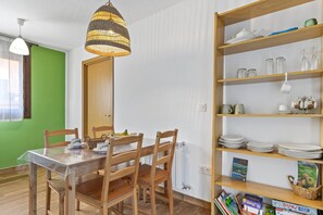 Un comedor con una mesa de madera, sillas, una lámpara colgante y una estantería con diversos objetos.