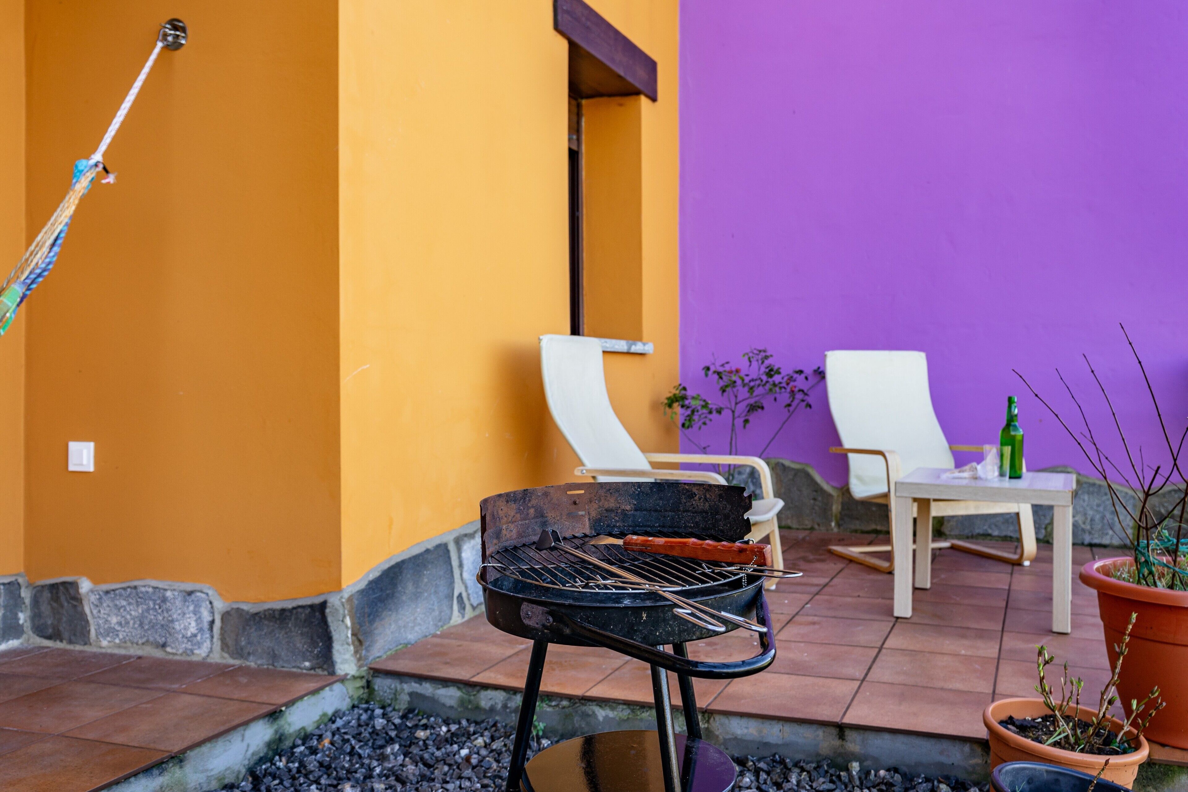 Un patio al aire libre con una parrilla, dos sillas blancas, una mesa y plantas en macetas.