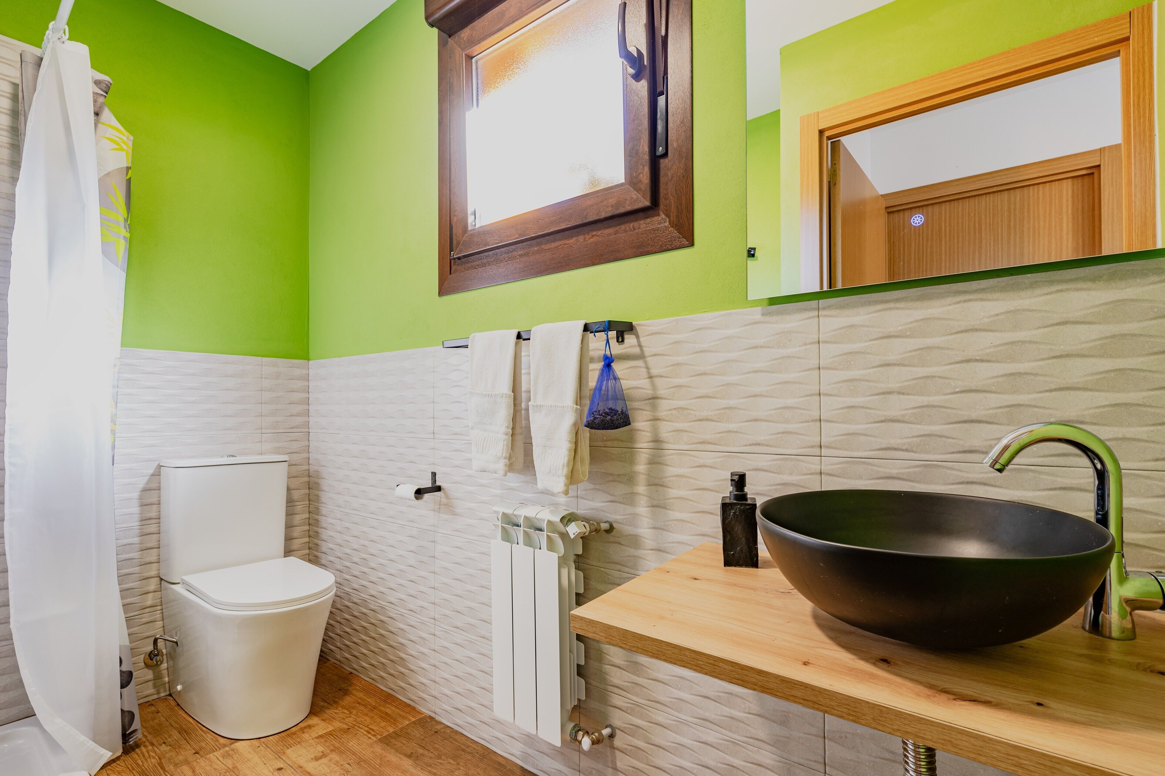 A bathroom with a toilet, a sink with a large basin, a towel rack, and a window with a wooden frame.
