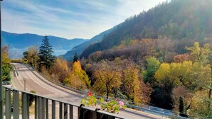 Uma estrada com guarda-corpo, cercada por árvores em tons de outono e um cenário montanhoso.