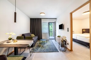 A modern hotel room with a sofa, dining table, and a TV.