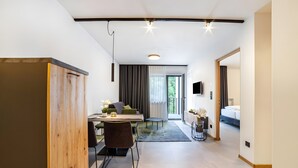 Quarto de hotel moderno com área de refeições, sofá, TV e uma grande janela.