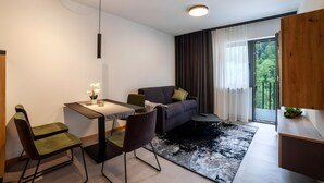 Ein modernes Wohnzimmer mit einer Couch, einem Esstisch, Stühlen, einem kleinen Teppich und Blick auf Grün durch ein Fenster.