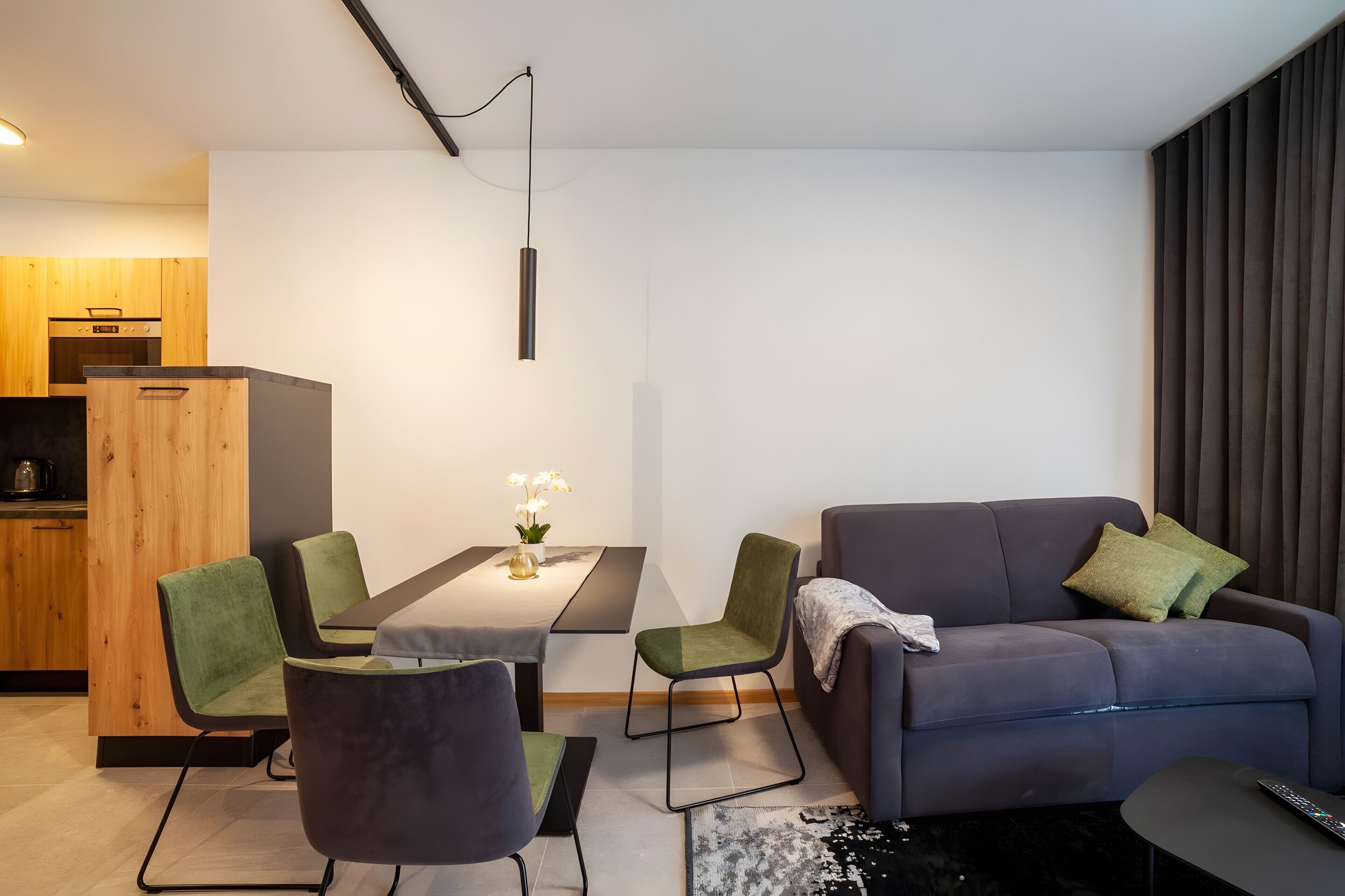 Un salon moderne comprenant une table à manger, des chaises, un canapé et un coin cuisine avec des meubles et des appareils électroménagers en bois.