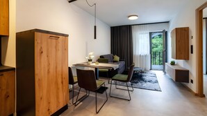 Eine moderne Küche mit Holzschränken, eine Essecke mit Stühlen, ein Sofa und Blick durch eine Glastür.