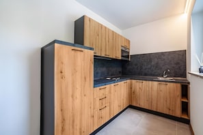 A modern kitchen with wooden cabinets, a black countertop, and a grey backsplash. - Apartment 'Pauli 3' with Mountain View, Shared Garden and Wi-Fi (Lagundo)