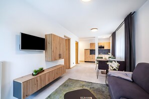 A modern living room with a flat-screen TV, wooden cabinets, a sofa, and a dining area with a table and chairs.