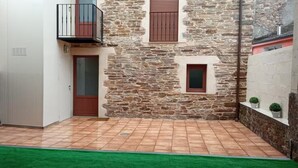 Un patio con muro de piedra, una puerta, una ventana y un pequeño balcón.