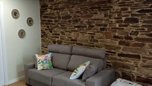 Una habitación con pared de piedra, un sofá gris con cojines de colores y tres platos decorativos colgados en la pared.