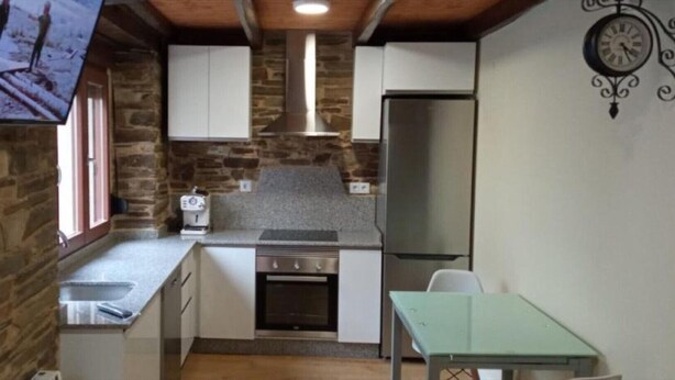 Una cocina compacta con pared de piedra, horno empotrado, refrigerador y una pequeña mesa de comedor.